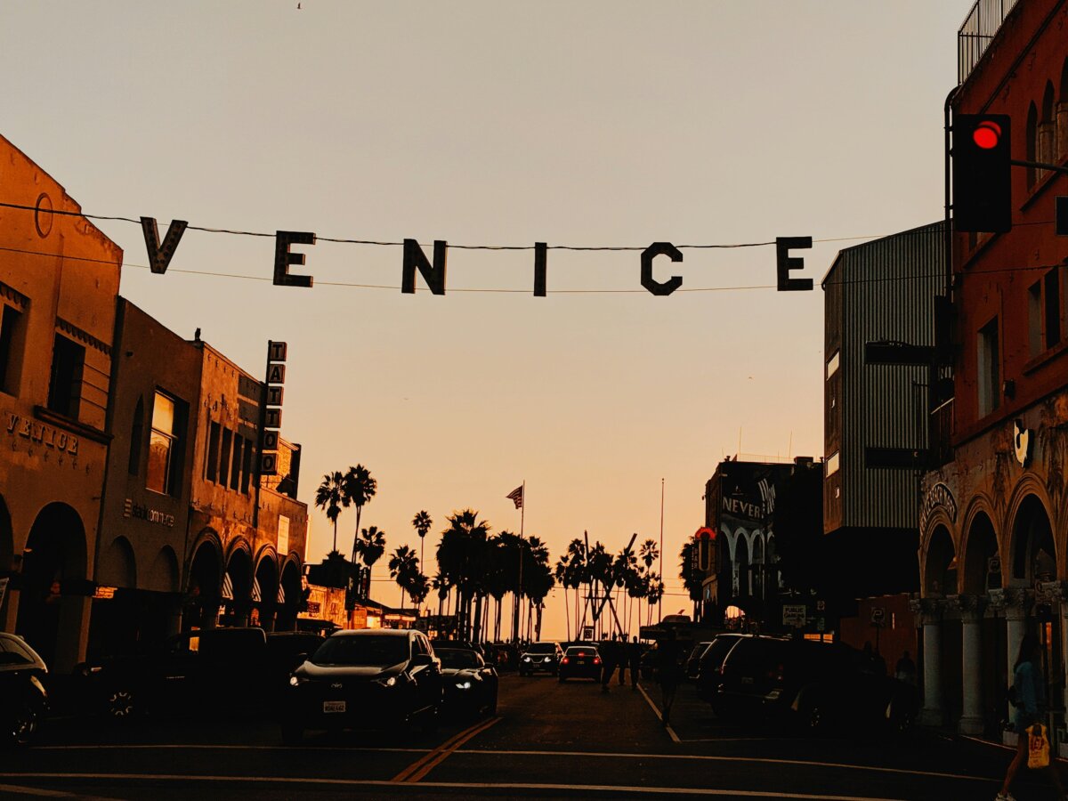 A city street at sunset, strung with a "VENICE" banner in Venice Beach, Los Angeles, California