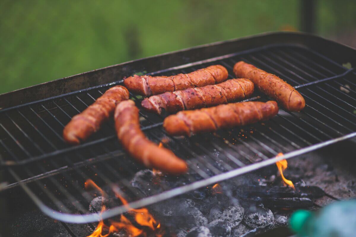 Bacon-wrapped hot dogs cooking over a charcoal grill